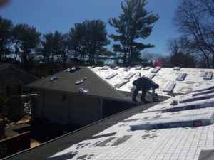 A man works on a shingle roof that is halfway completed.