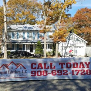 A two-story house with a banner in front of it that says, "Elegant Exteriors, LLC Roofing, Siding & Windows. Call Today".
