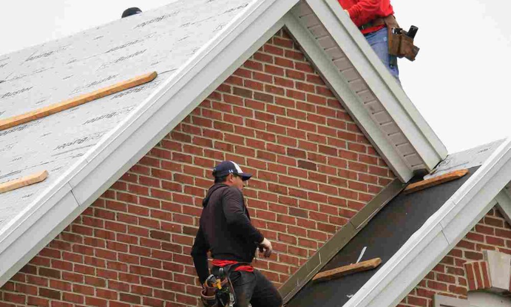 Two men collaborating on a rooftop, engaged in construction work under clear skies.