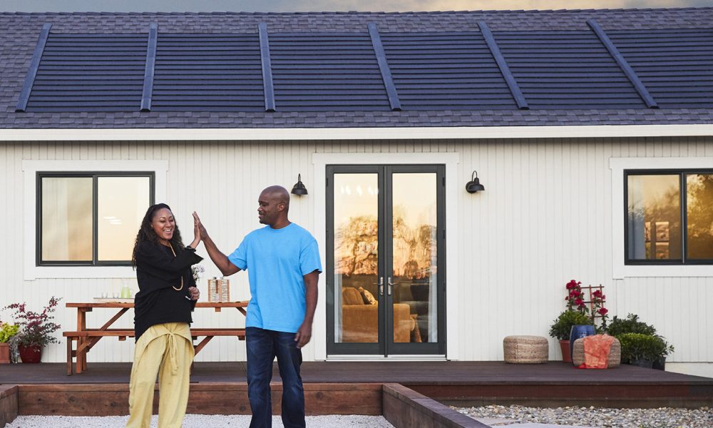 A happy couple standing outside their home with Timberline Solar™ Shingles installed on the roof, celebrating their new energy-efficient roofing system.