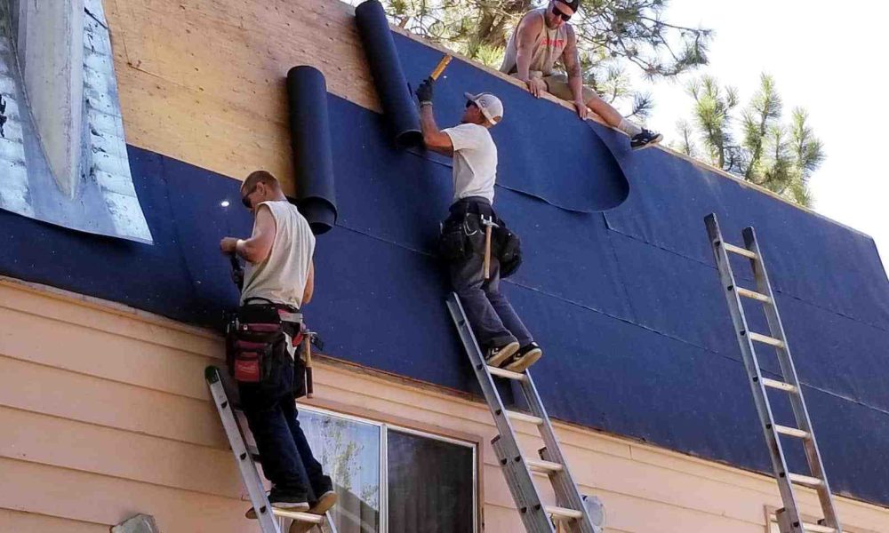 Two men are collaborating on a roof, utilizing a blue tarp for protection against the elements.