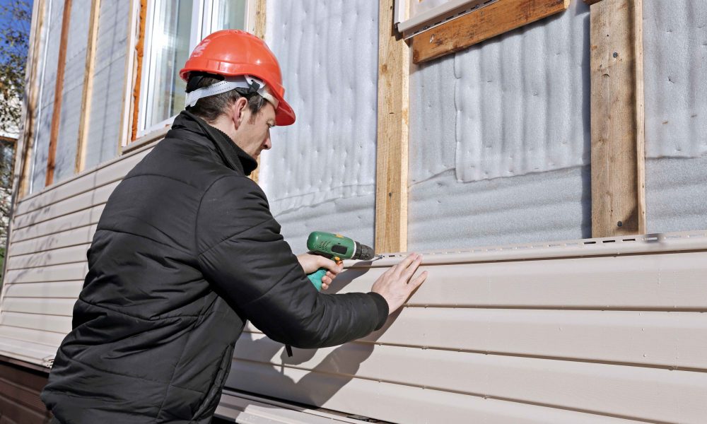 A worker installs panels beige siding on the facade of the house